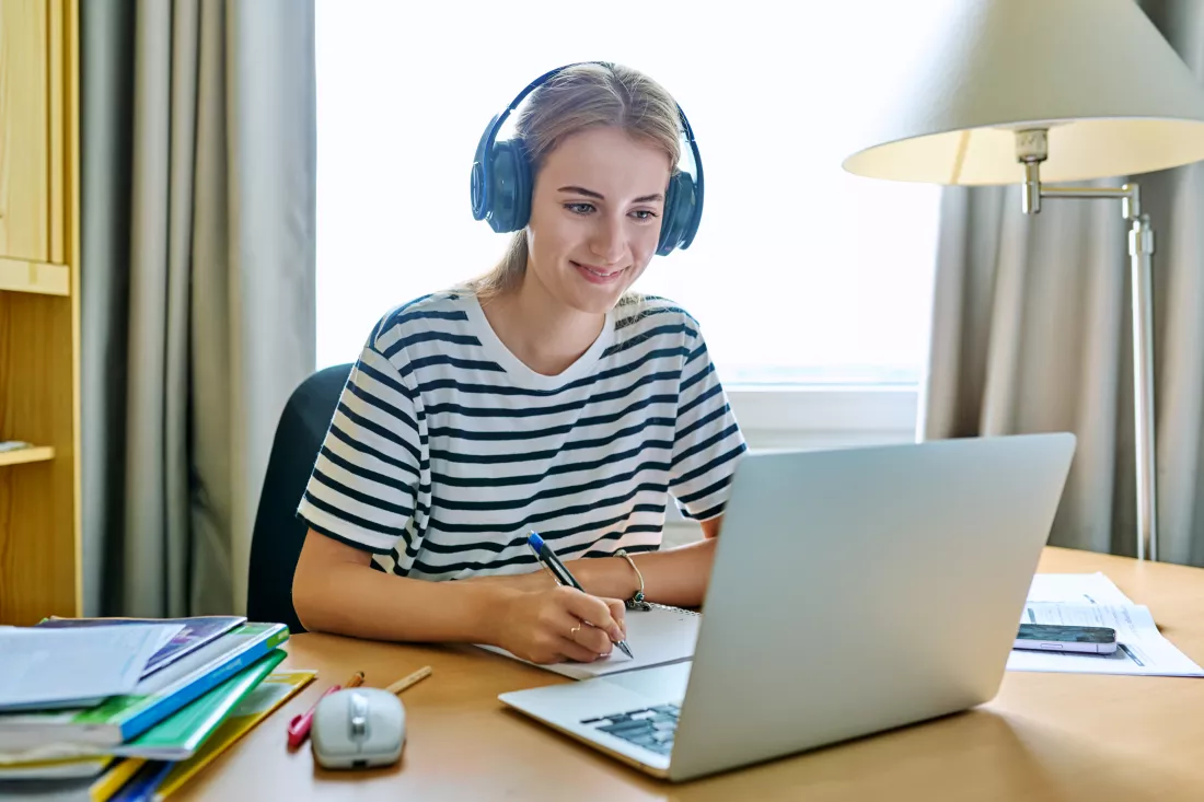 girl-teen-student-headphones-sitting-desk-using-computer-writing-study-notebook